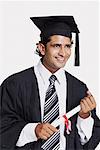 Close-up of a male graduate holding a diploma and smiling