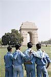 Rear view of four boys standing with their arms around each other in front of a monument, India Gate, New Delhi, India