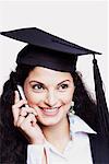 Close-up of a female graduate using a mobile phone and smiling