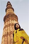 Low angle view of a young woman standing in front of a monument, Qutub Minar, New Delhi, India