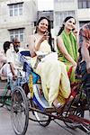 Two young women sitting in a rickshaw and using mobile phones