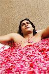 Close-up of a young man lying in a bathtub filled with rose petals