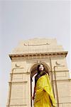 Low angle view of a young woman standing in front of a monument, India Gate, New Delhi, India