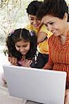 Gros plan d'une femme mature et ses deux petits-enfants regardant un ordinateur portable