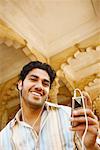 Portrait of a young man holding an MP3 player and listening to music on headphones, Agra Fort, Agra, Uttar Pradesh, India