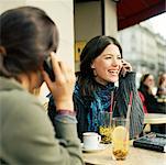 Two teenage girls sitting at cafe terrace, holding cell phones