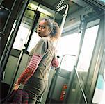 Young woman holding rail, getting on bus, looking back over shoulder