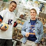 Young men leaning against store window, smiling, facing camera.