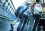 Group of young people walking down sidewalk with backpacks, low angle, rear view