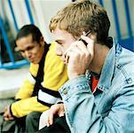 Young men sitting together, close up of one on cell phone, side view