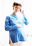 La femme enceinte à l'aide d'un téléphone cellulaire, souriant à la caméra, portrait