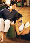 Man sitting backwards on chair and pregnant woman sitting on floor, reading and leaning head on man, portrait