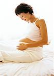 Pregnant woman sitting on bed, looking at her stomach