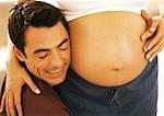 Man pressing cheek to pregnant woman's stomach, close-up