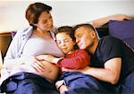 Schwangere Frau mit Mann und Kind im Bett sitzen