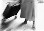 Woman pulling shopping cart, low section, blurred, b&w