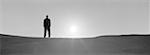 Man standing on sand, backlit by sun, b&w, panoramic view
