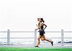 Couple jogging, sea in background, side view.