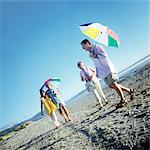 Deux couples matures, debout sur la plage, hommes tenue parapluies
