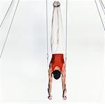 Young male gymnast doing handstand on rings, rear view.