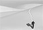 Man hiking up sand dune, rear view, b&w