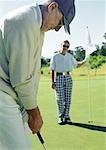 Zwei ältere Golfer spielen, Einlochen, der andere Betrieb-Flagge