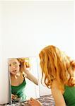 Woman looking at reflection in mirror, pulling her hair back.
