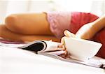 Woman lying on bed, mid-section, blurred, with magazine and bowl in focus in foreground, close-up.