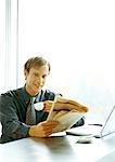 Businessman sitting at desk, drinking and reading