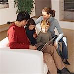 Family sitting together on sofa, looking at laptop