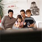 Family sitting on the couch, rear view of tv in foreground, blurred