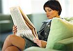 Femme assise avec les jambes croisées, lisant journal d'affaires