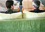 Businessmen sitting side by side with newspapers, rear view