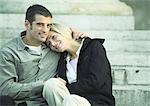 Couple sitting together on stairs, woman leaning head on man's shoulder