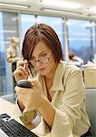 Geschäftsfrau Anpassung Brille betrachten Telefon, im Büro, hautnah.
