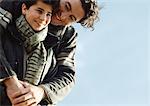 Adult man with arms around boy from behind, both in warm clothes, portrait, close up, sky in background