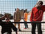 Men standing behind fence in urban playground