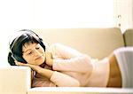 Woman lying on sofa, listening to headphones