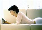 Woman lying on sofa, reading