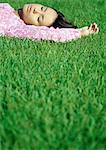 Woman lying on grass with eyes closed, surface level view