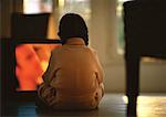 Young girl sitting on floor watching TV, rear view