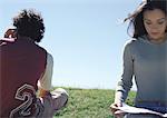 Young couple sitting together on grass facing in opposite directions