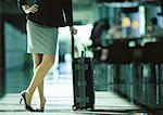 Femme d'affaires s'appuyant sur une valise avec ses jambes croisées, partie inférieure