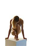 Nude woman with head down crouching on pedestal, front view