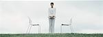 Woman standing outdoors on grass between two chairs in front of overcast sky