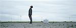 Man standing in abandoned lot looking up at sky, metallic briefcase on ground behind him