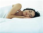 Woman lying on side on bed with hands under head and eyes closed