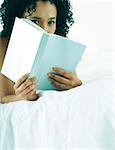 Woman lying on stomach on bed, reading book