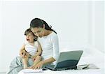 Woman sitting on bed with little girl on lap crying, looking down at paper