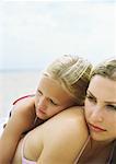 Girl leaning against mother's back on beach